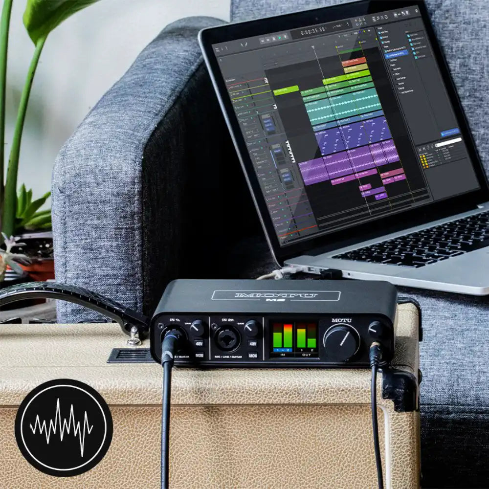 Laptop with music production software on a couch next to MOTU M2 audio interface.