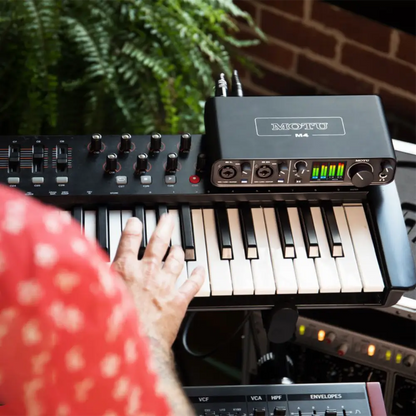 MOTU M4 USB-C Audio Interface on keyboard with hands playing, showcasing professional music production setup.
